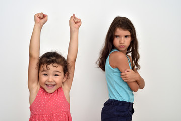 Happy and smiling cute young girl with hands up and her jealous and angry older sister. Focus on...