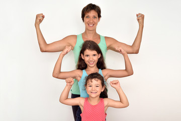 Fototapeta na wymiar Strong smiling mother and her two cute daughters standing behind each other and showing their strong arms 