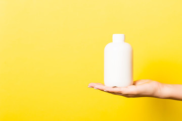 Female hand holding cream bottle of lotion isolated. Girl give tube cosmetic products on yellow background