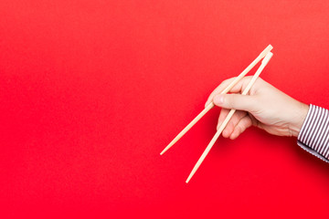 Wooden chopsticks holded with male hands on red background. Ready for eating concepts with empty space