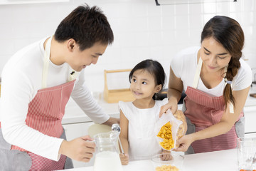 Happy Asian family make a cooking. Father and Mother make breakfast, cereal with milk give daughter in the kitchen at home. Healthy food concept For the strength of the body