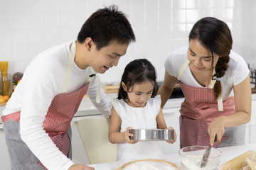 Happy Asian family Father, Mother and Daughter are sieving flour preparing the dough, bake cookies in the kitchen. family cooking food Concept.
