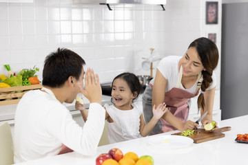 Obraz na płótnie Canvas Happy Asian family make a cooking. Father, Mother and Daughter are preparing fruit, green apple in the kitchen at home. Healthy food concept and happy holidays