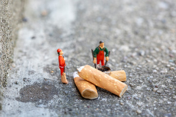Two miniature garbage men cleaning and sweeping smoked cigarettes on the street which pollute the...