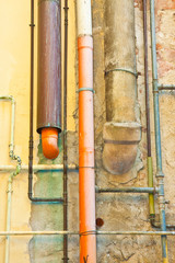 Old hydraulic system with an orange polypropylene exhaust pipes and copper and metal pipes against an old plaster wall