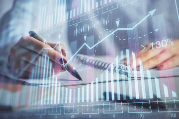 Double exposure of woman's hands making notes with forex graph hologram. Concept stock market analysis.