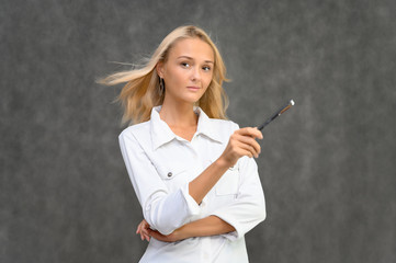 Studio portrait of a pretty blonde student girl, young woman in a white shirt on a gray background. Talking, showing emotions.