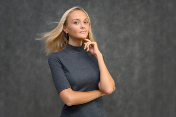 Fototapeta premium Studio portrait of a pretty blonde student girl, young woman in a gray sweater on a gray background. Talking, showing emotions.