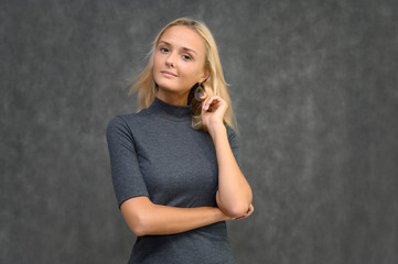 Studio portrait of a pretty blonde student girl, young woman in a gray sweater on a gray background. Talking, showing emotions.