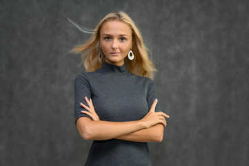 Studio portrait of a pretty blonde student girl, young woman in a gray sweater on a gray background. Talking, showing emotions.