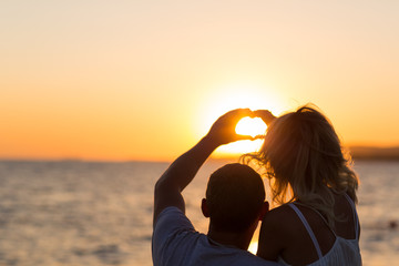 Back view of a couple silhouette hugging and watching sun on the beach