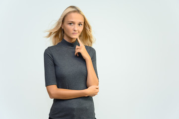 Studio portrait of a pretty blonde student girl, young woman in a gray sweater on a white background. Talking, showing emotions.