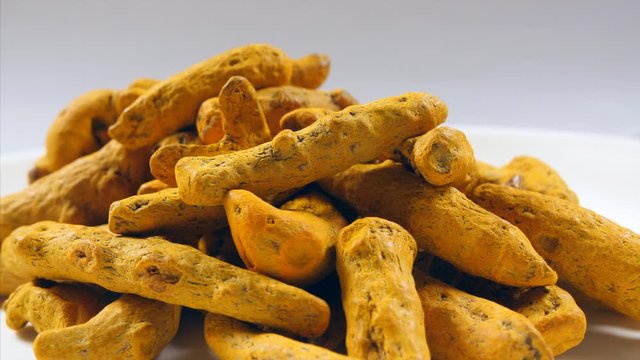 Close shot of dry turmeric roots (Authentic Indian Spice) rotating on a white table. 