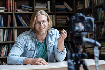 Young male influencer tutor teacher blogger talking looking at professional dslr camera shooting...