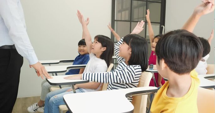 Asian teacher teaching children in the classroom at school. Little boy and girl raise hands together for accepting comments. Concept of education, experience learning and skill development.