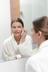 Woman holding cream in hands, standing at bathroom