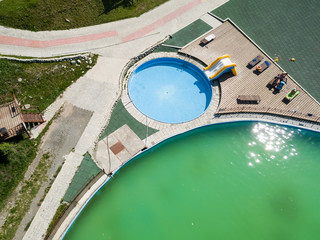 Aerial view of a tourist recreation center with a children's pool with blue clear water, an inflatable slide and wooden sun loungers. Rest, tourism and vacation.