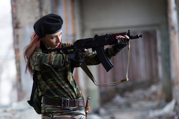 Soldier girl with weapons in camouflage uniform in a destroyed building. The concept of service in...