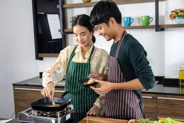 A young man and a beautiful Asian teenager is happy to make shrimp salad in a modern kitchen.