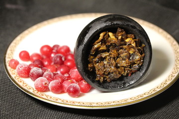 bowl with tobacco for hookah. berries on a black background. smoking hooka