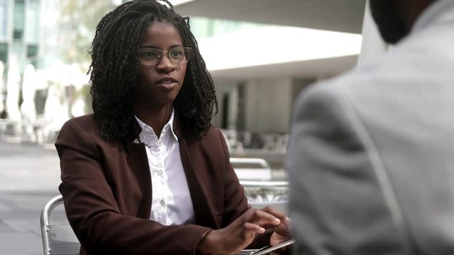 Confident business consultant talking with client at cafe. African American woman with dreadlocks talking with colleague while using tablet. Business concept