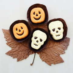 Funny Halloween jack-o-lantern and skull shaped shortbread sandwich cookies. dry autumn leaves.