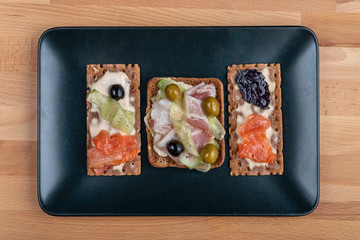 toasts with bacon, cheese and salmon on a dark plate on a wooden background