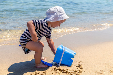 Baby boy on the beach with blue bucket, children concept