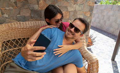 Lovely happy couple together hugging and laughing enjoying the embracing and tenderness. Lovers sitting and taking a selfie with smart phone, touching and relaxing with pleasant. Husband and Wife