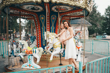 a little girl with her mother riding in the Park on a toy horse on the carousel. Entertainment industry concept, family day, children's parks, playgrounds