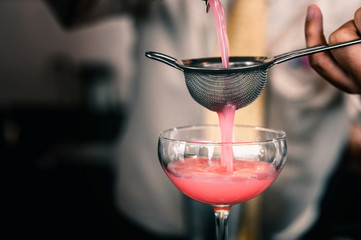 Barman is making pink cocktail at night club.