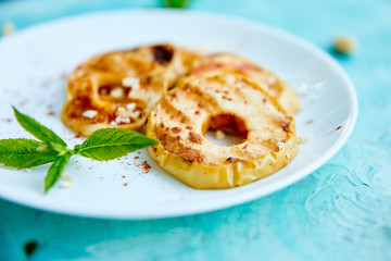 Grilled apples with cinamon on white plate on blue background. Grilled dessert. Barbecue fruit. Copy space. Healthy food. Vegan food.