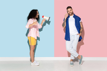 Fototapeta premium Young emotional caucasian couple in bright casual clothes posing on pink and blue background. Concept of human emotions, facial expession, relations, ad. Woman screams with mouthpeace, man ignores her