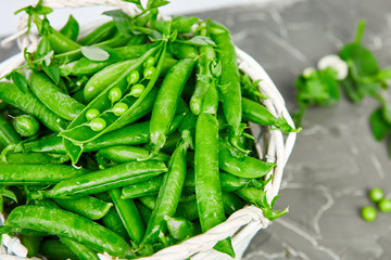 White Basket with fresh green peas on grey background. Vegan and vegetarian food concept. Flat lay.