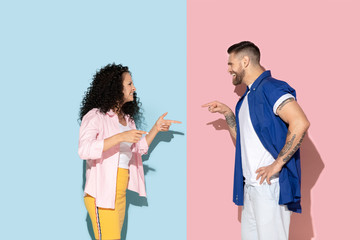 Young emotional caucasian couple in bright casual clothes posing on pink and blue background. Concept of human emotions, facial expession, relations, ad. Man and woman abusing, swearing and pointing.