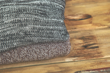 Stack of cozy knitted sweaters. A pile of warm sweaters on a wooden table on rustic background. Autumn and winter clothes. Copy space. Flat lay