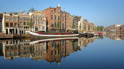 Crooked and colorful heritage buildings and houseboats, overlooking Amstel river with perfect reflections, Amsterdam, Netherlands
