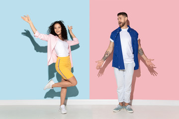 Naklejka premium Young emotional caucasian couple in bright casual clothes posing on pink and blue background. Concept of human emotions, facial expession, relations, ad. Man is bored, woman dancing and celebrating.