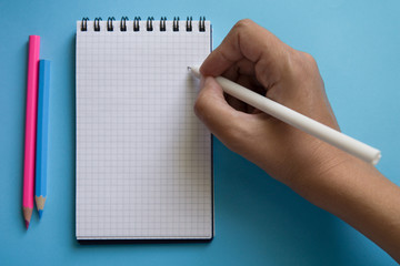 Woman hand writing in blank notebook on a two color background. Trendy pink and blue colors. Back to school concept. Mock up, flat lay.