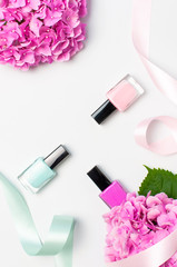 Obraz na płótnie Canvas Decorative cosmetics, nail polish. Set of different varnishes for manicure nails on light background with flowers of pink hydrangea top view Flat lay mock up. Female cosmetics. Beauty blogger concept
