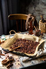 homemade baked chocolate granola with nuts, oat flakes on baking tray with parchment stands on grey wooden table