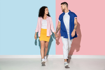 Obraz premium Young emotional caucasian couple in bright clothes posing on pink and blue background. Concept of human emotions, facial expession, relations, ad. Man and woman holding hangs and going, smiling.