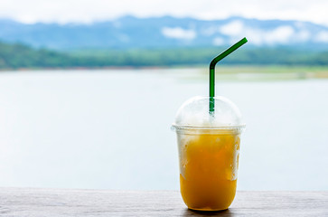 Glass of cold Orange juice smoothie on the table Background blurry views sky water and mountain.