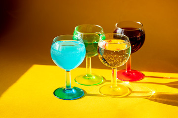Multi-colored liquor in glasses in the sun on a yellow background