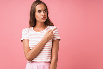 Image of disappointed young woman wearing striped clothes frowning and pointing finger aside at copyspace