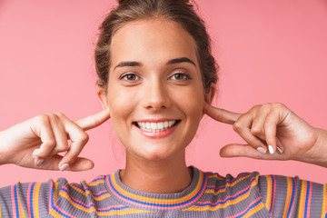 Image closeup of pleased beautiful woman dressed in colorful clothes smiling and plugging her ears...