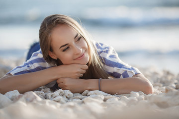 Beautiful brunette sitting on the rocks.Sexy brunette girl posing alone on the beach in the evening.Young pretty hot sexy attractive girl relaxing in in a striped shirt and shorts on stones with blue 