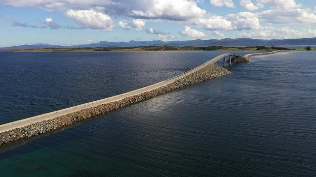 Aerial drone shot over the ocean of a road with a bridge leading through the water. Crossing the sea by car, island to island.