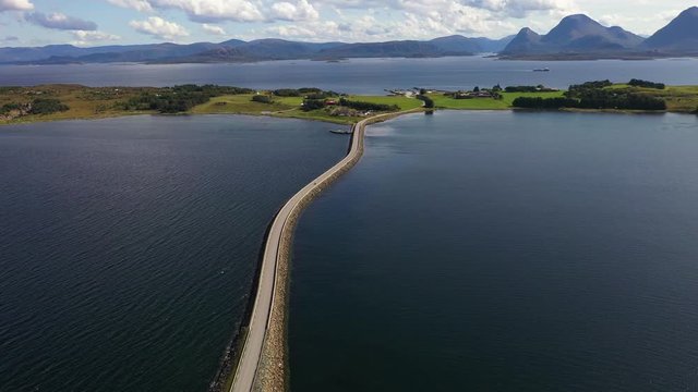 Aerial drone push in shot over a road on the ocean, drivers to an island. Car drives away from the island.