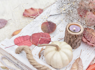 autumn still life. Colorful leaves, candle and white mini pumpkin on a light wooden tray. Selective soft focus.